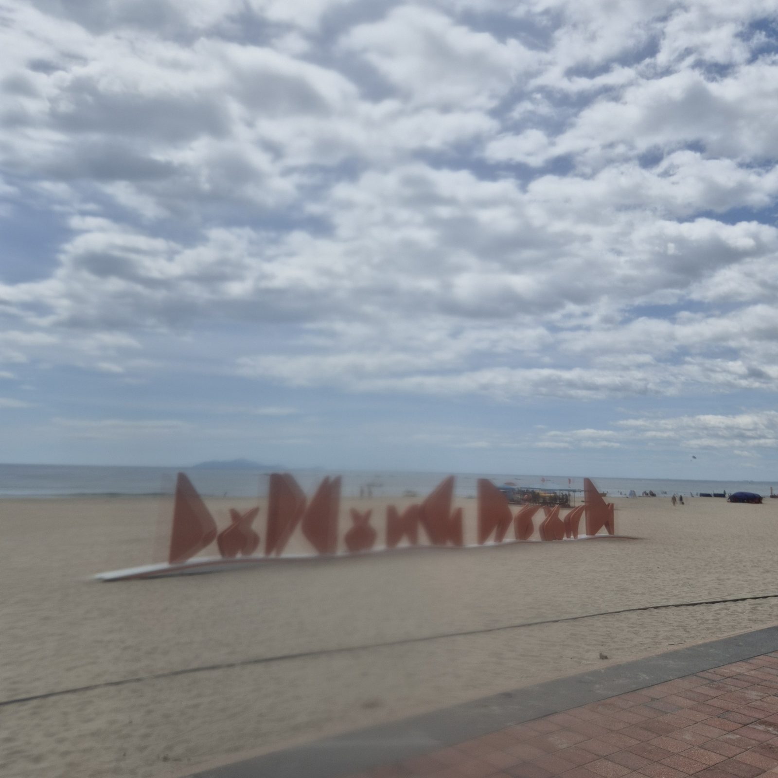 미케 해변 모래사장 위의 빨간 DA NANG BEACH 대형 글씨 조형과 바다·섬 능선이 보이는 다낭 비치 랜드마크
